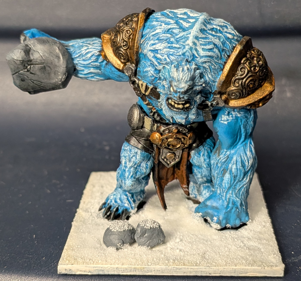 Mantic Ice Troll painted blue with white highlights on a snow base. The troll has a rock in hand at shoulder level.